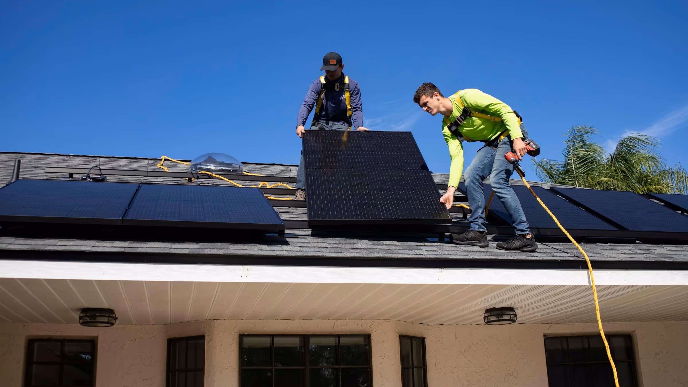 Two workers installing solar panels on a rooftop against a clear blue sky.