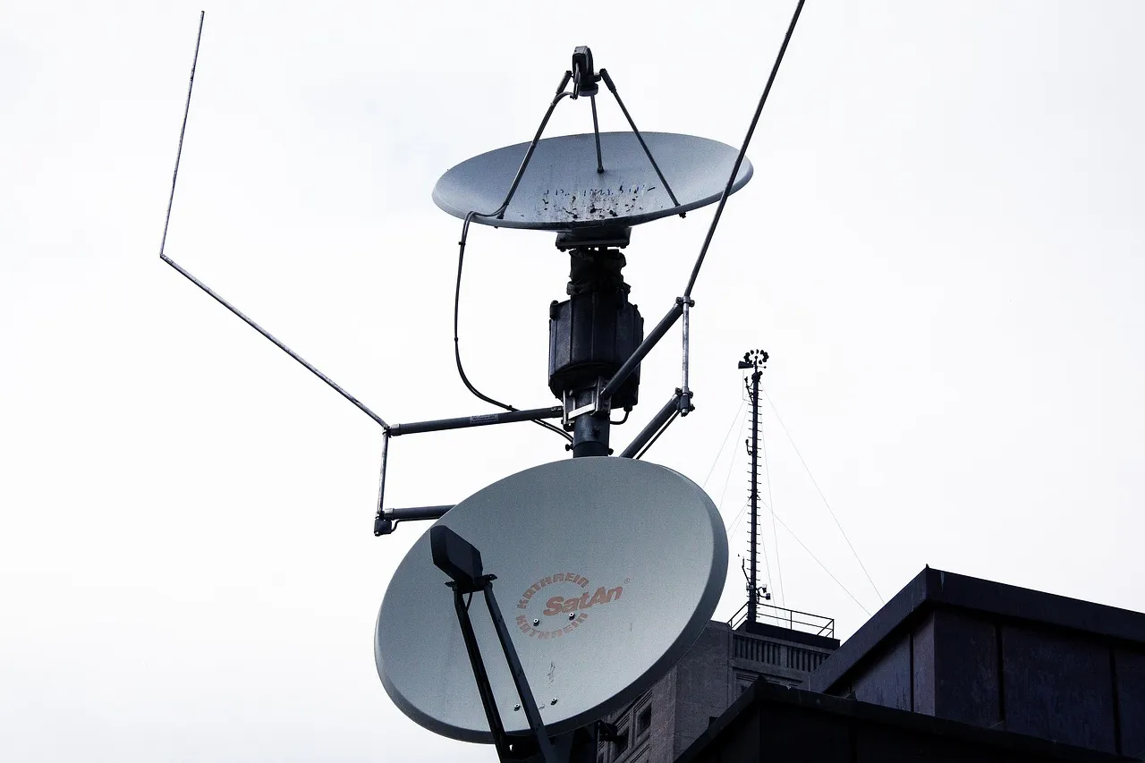 Two satellite dishes mounted on a rooftop against a cloudy sky backdrop.