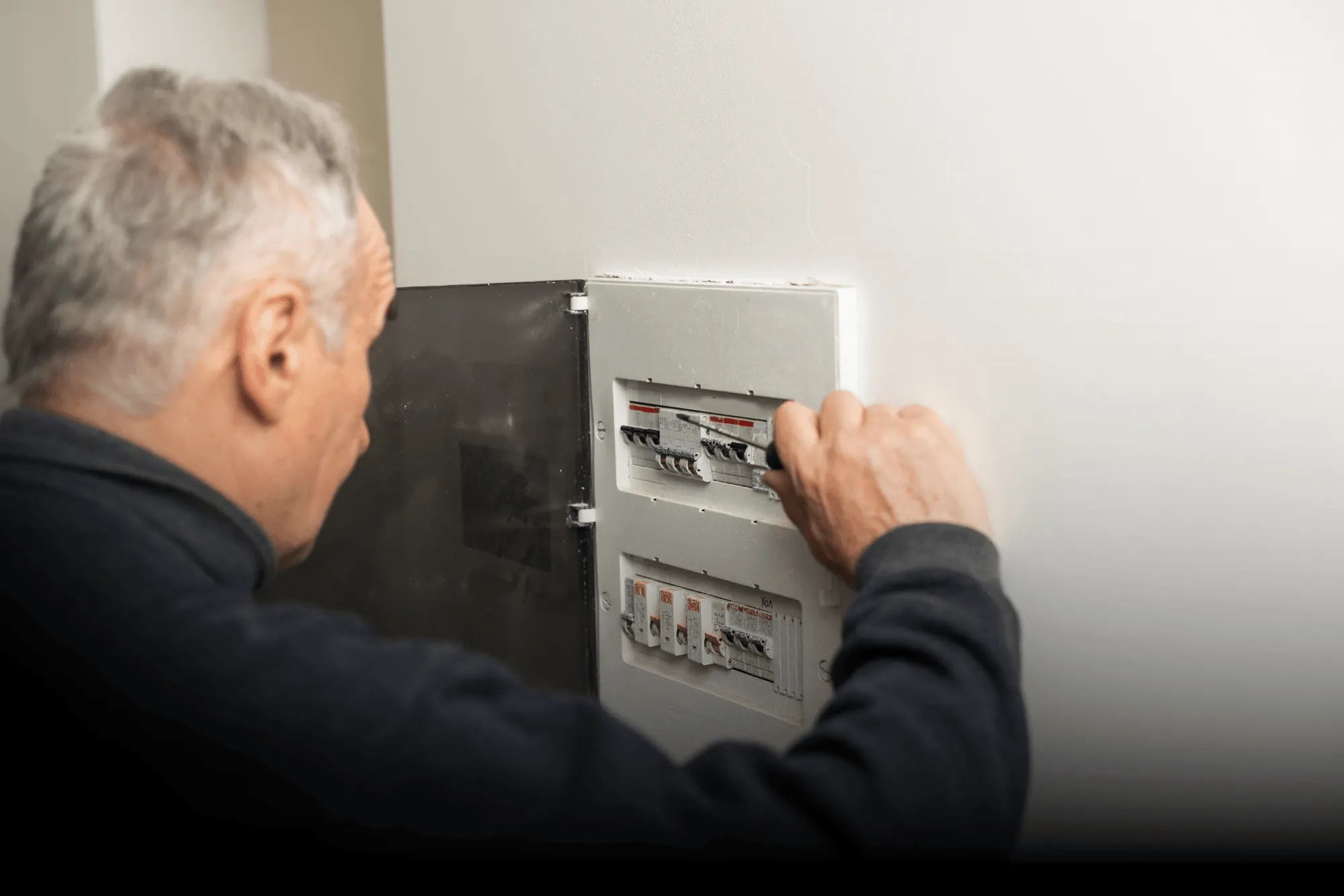 Man adjusting switches on an open electrical breaker panel mounted on a wall.
