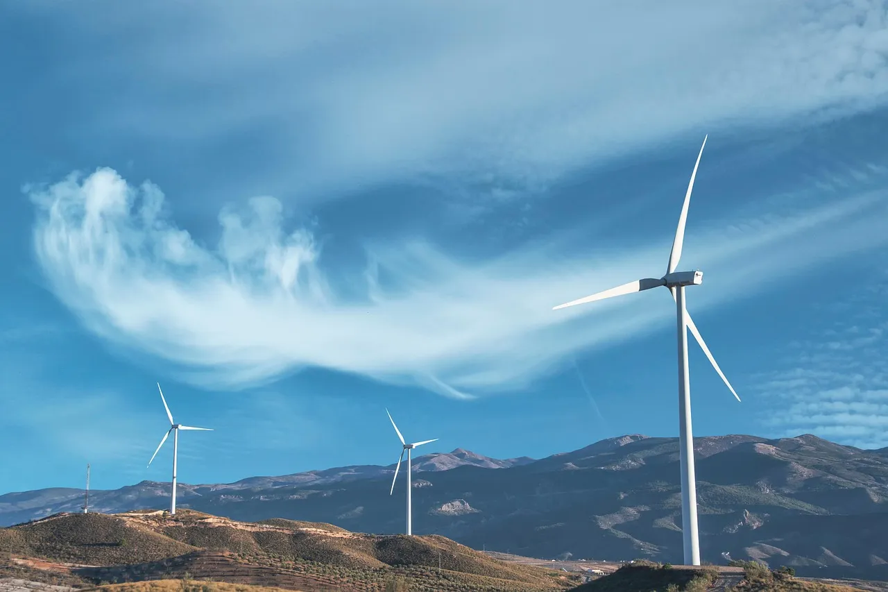 Three white wind turbines on hilly terrain under a blue sky with wispy clouds.