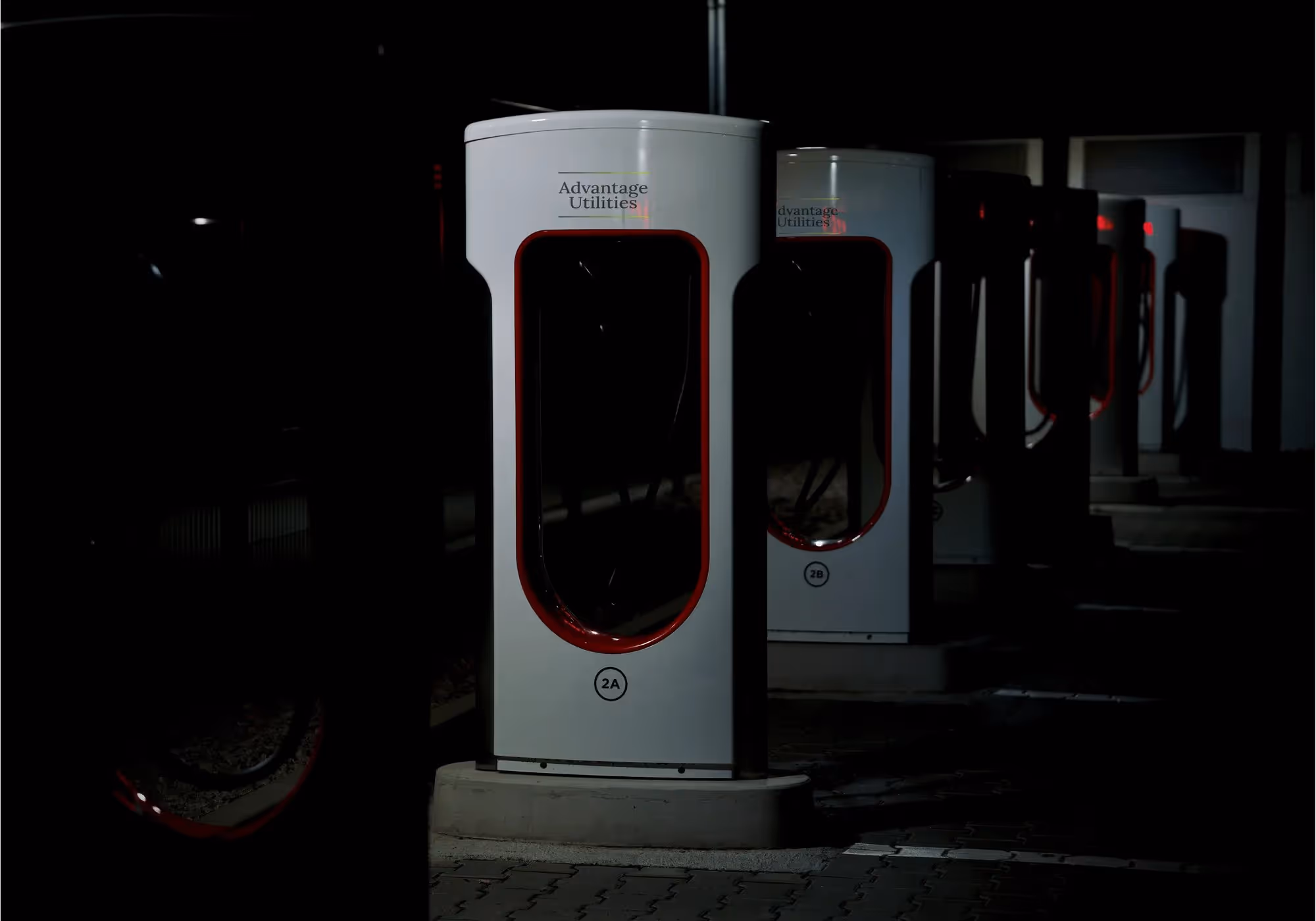 Row of unoccupied electric vehicle charging stations labeled Advantage Utilities at night.
