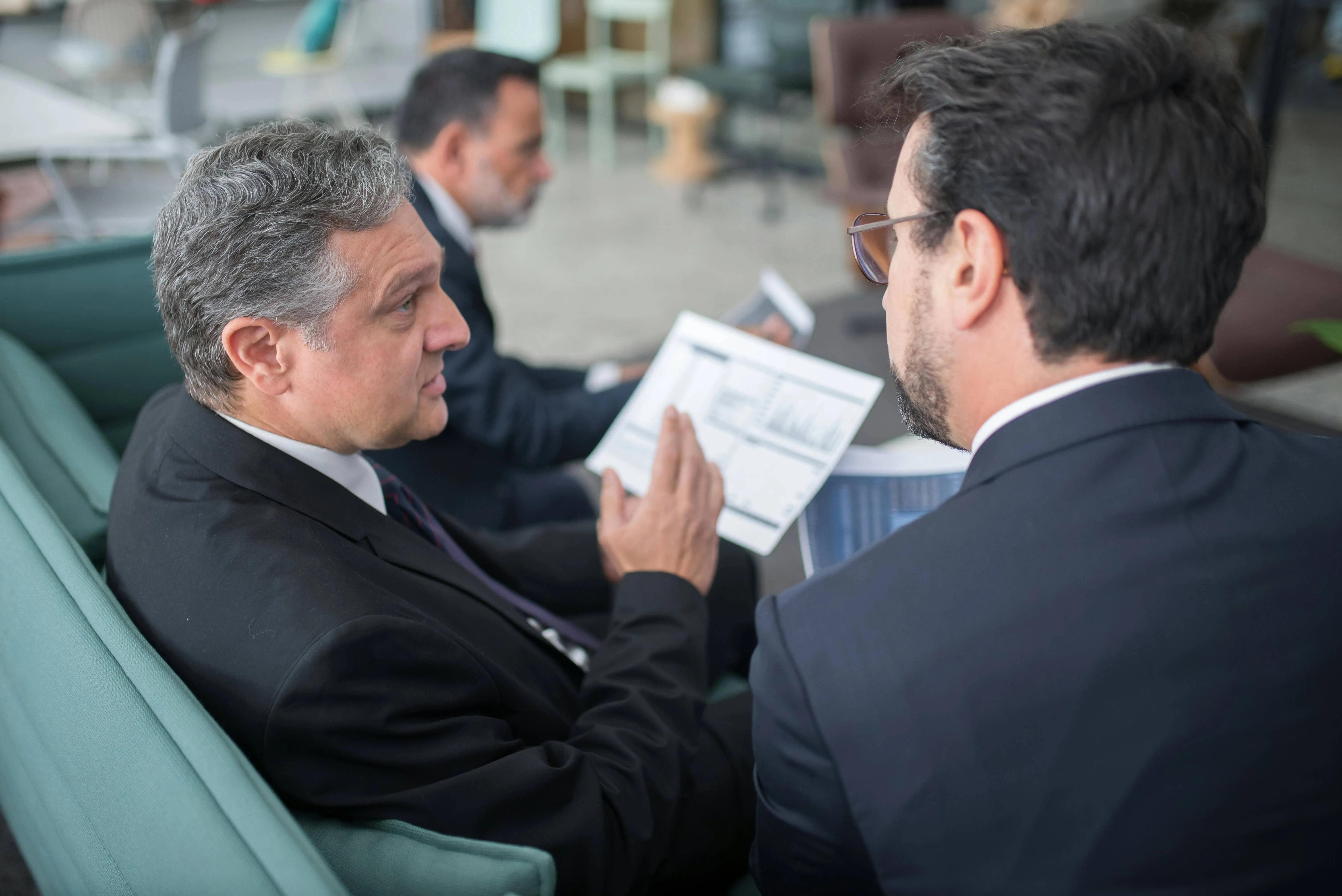 Two businessmen in suits reviewing financial charts and documents during a discussion in an office.