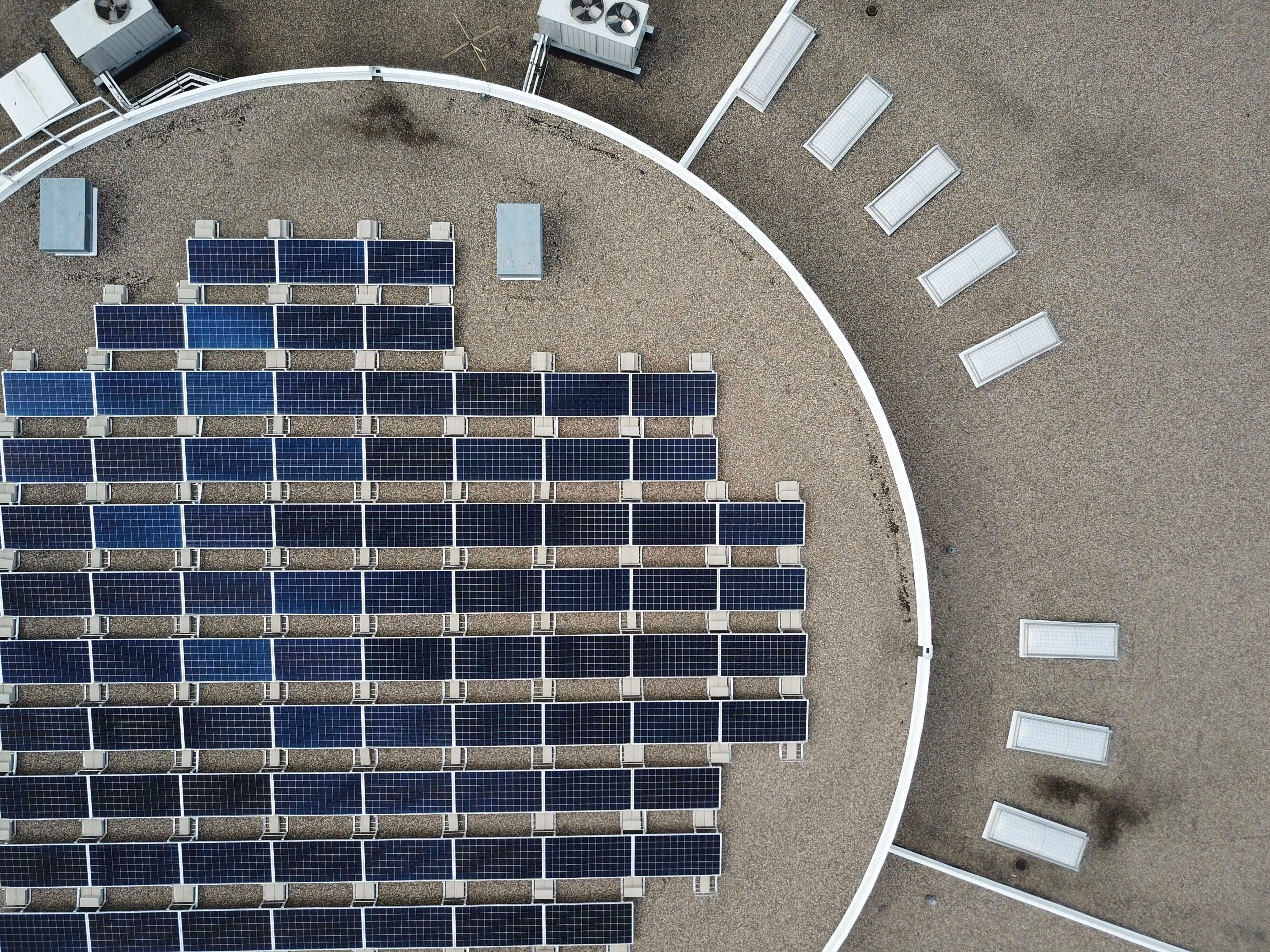 Aerial view of solar panels installed on a gravel rooftop of a circular building section.