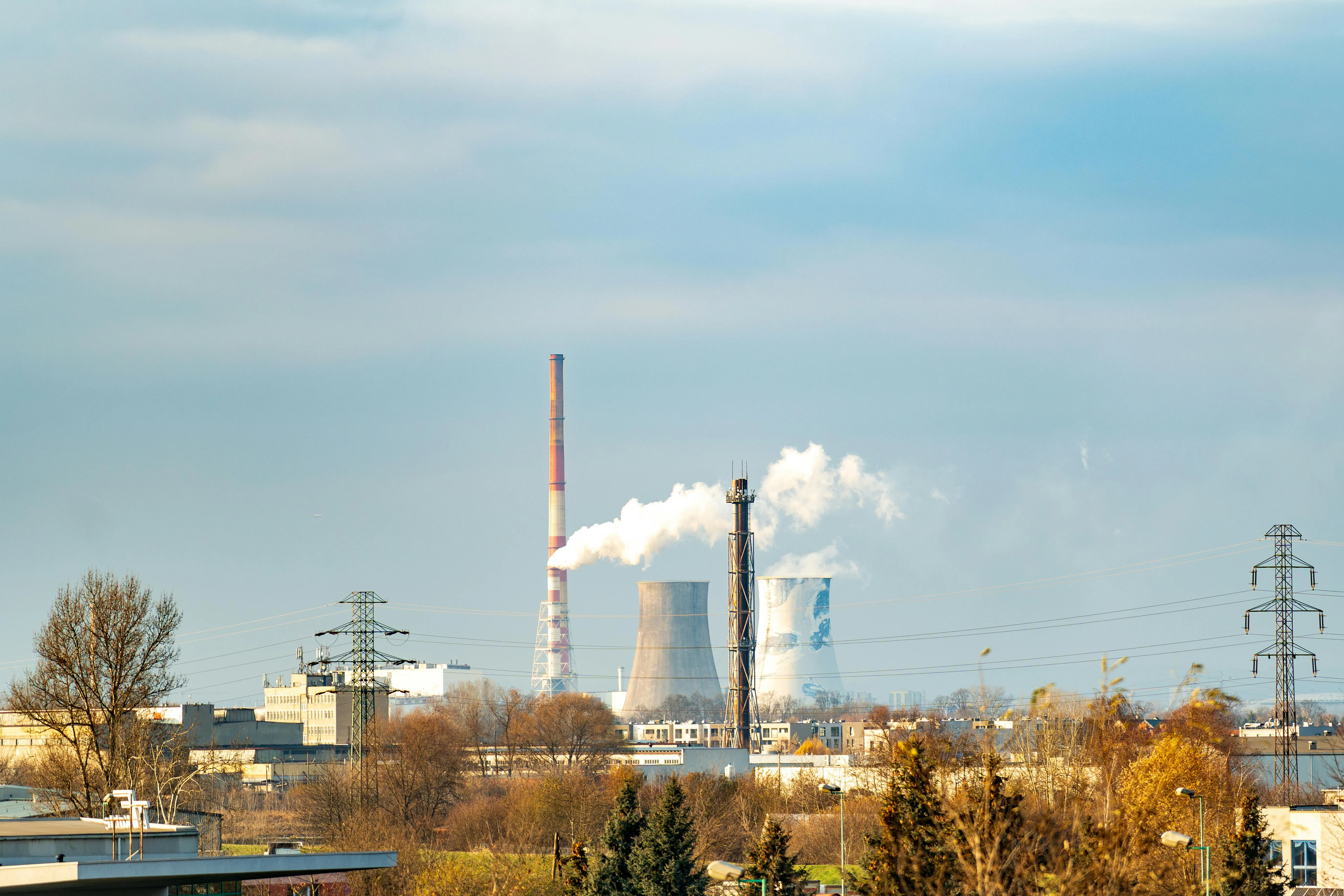 Industrial power plant with cooling towers emitting white steam and electrical transmission towers during daytime.