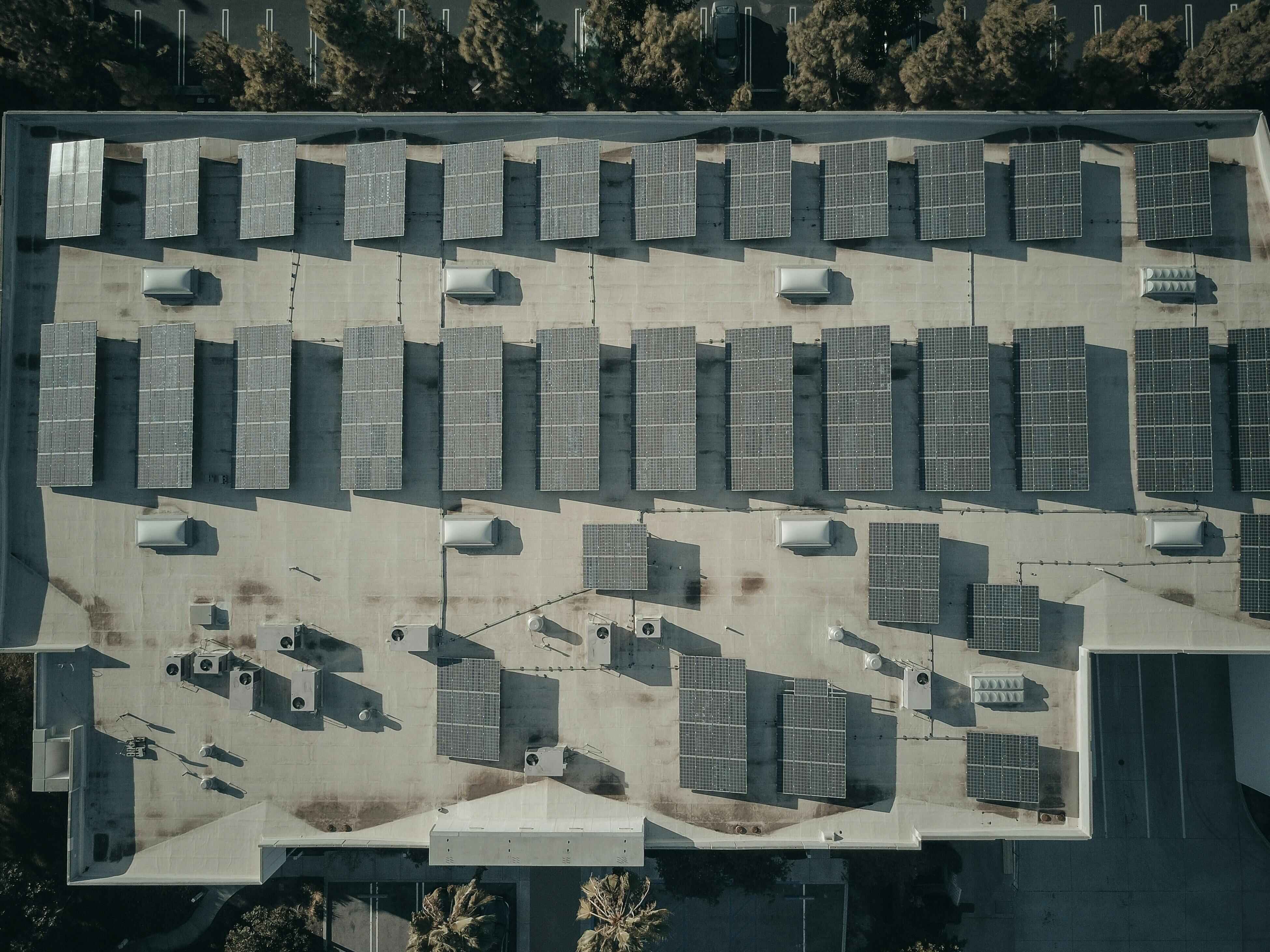 Aerial view of a flat rooftop covered with multiple solar panel arrays and HVAC units.