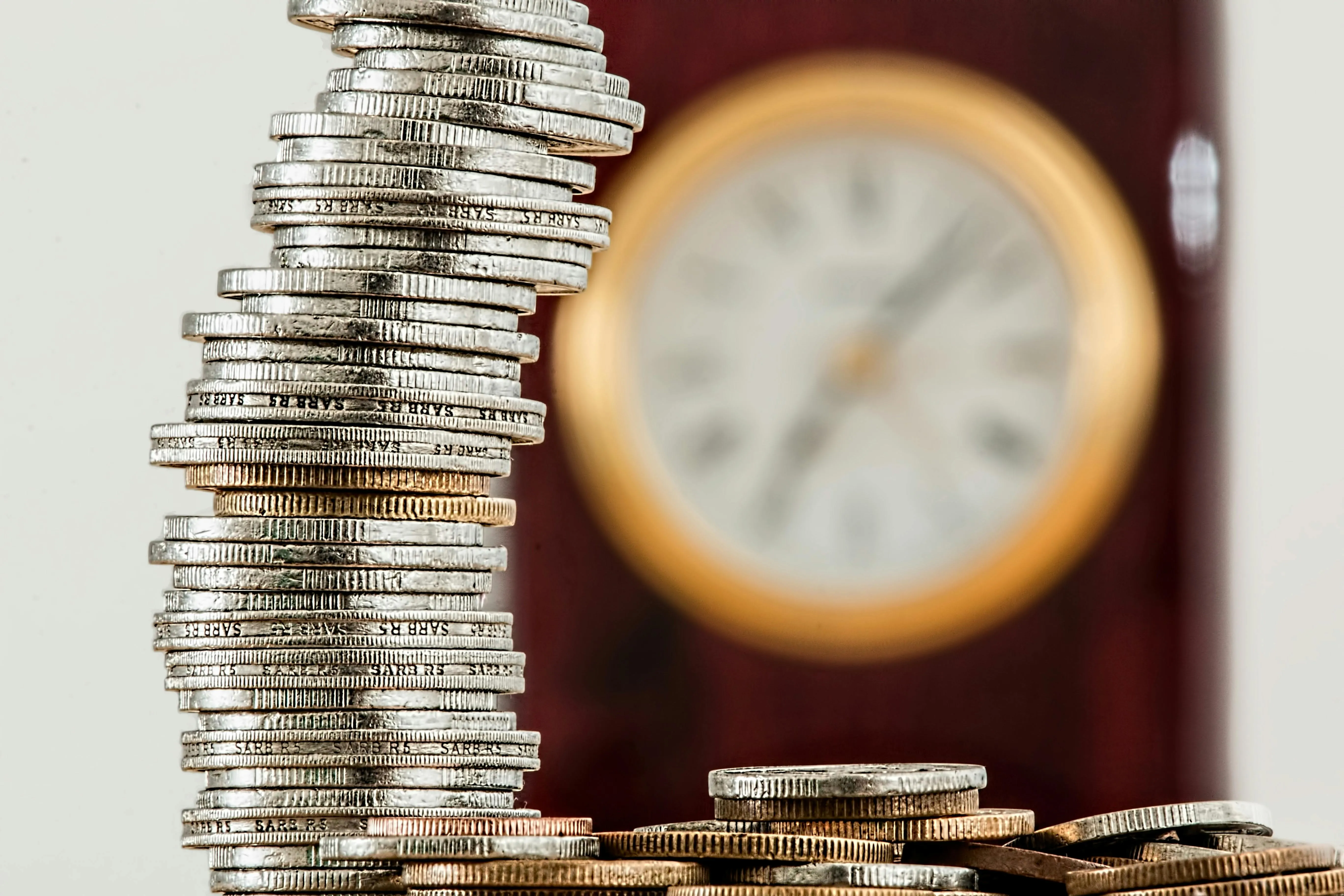 Stacked silver coins forming an arch with a blurred clock in the background.