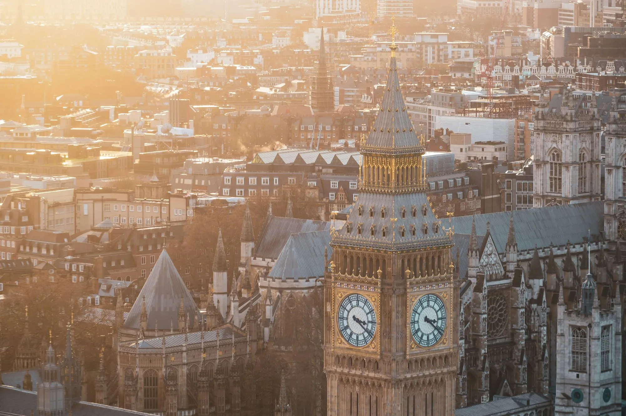 Golden hour view of London with the Big Ben clock tower prominently in the foreground and surrounding historic buildings.