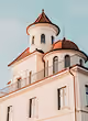 White building with classical architecture and a round dome with a small cross on top against a pale sky.