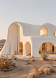 Modern white adobe-style house with curved walls and arches at sunset in a desert landscape.