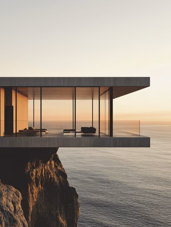 Modern glass house with furniture perched on a cliff overlooking a calm ocean at sunset.