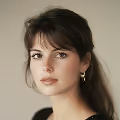 Portrait of a young woman with brown hair, bangs, and hoop earrings against a neutral background.