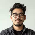 Portrait of a young man with glasses, mustache, and beard wearing a black shirt against a plain light background.