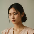 Portrait of a woman with dark hair in a low bun wearing a beige top against a neutral background.
