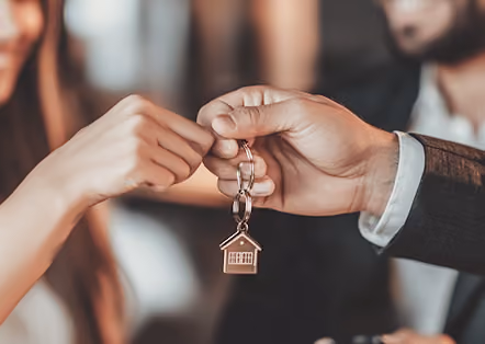 Two hands exchanging a keychain with a small house-shaped charm.