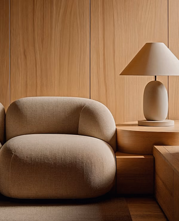 Modern beige upholstered armchair next to a wooden side table with a beige ceramic table lamp.