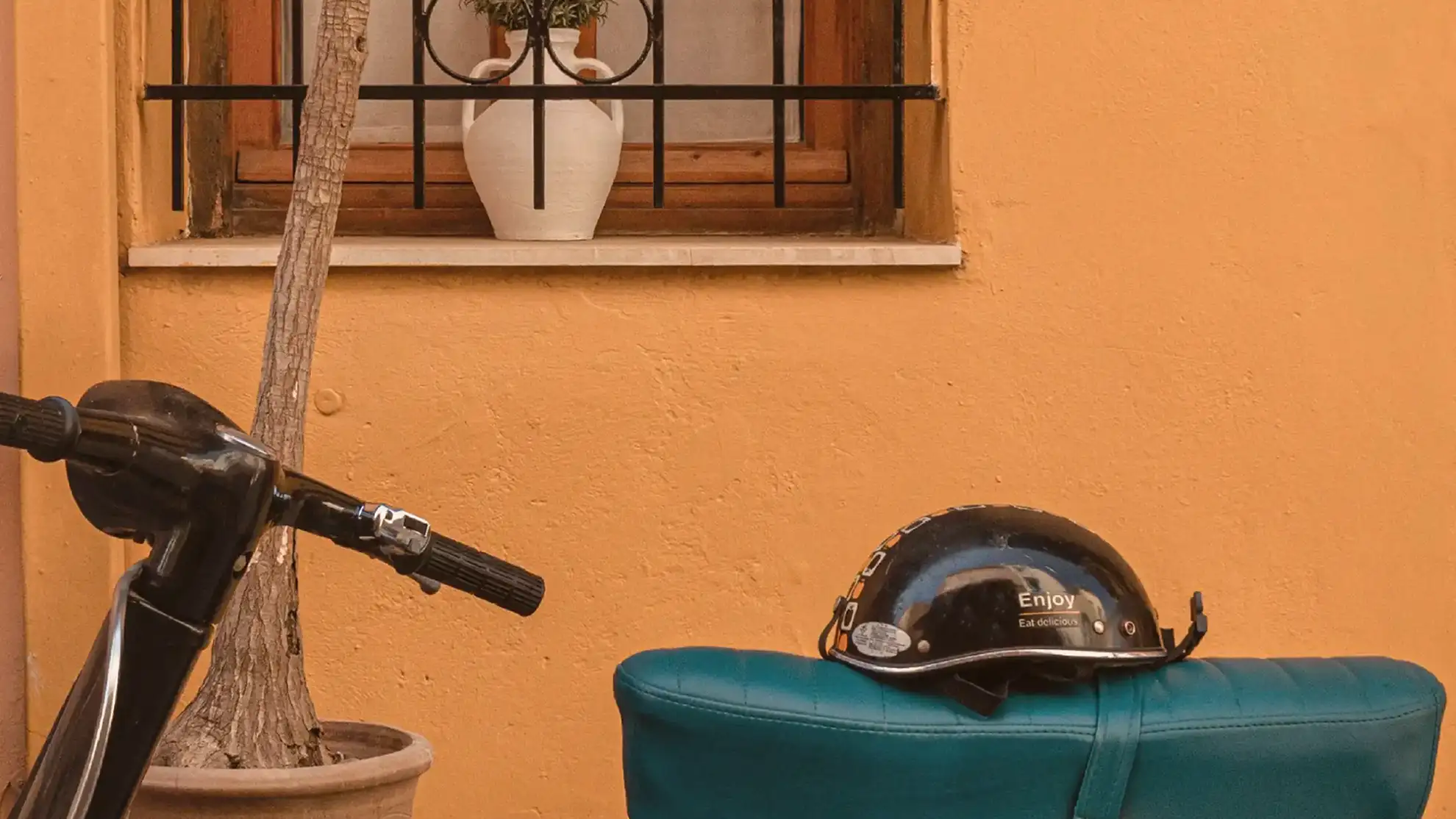 An old scooter in front of an orange wall and a palm tree.