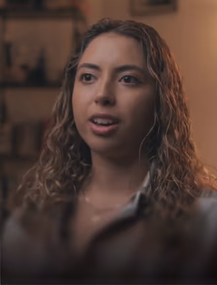 Smiling man with short dark hair wearing sunglasses on his head and a colorful striped shirt, outdoors with trees in the background.