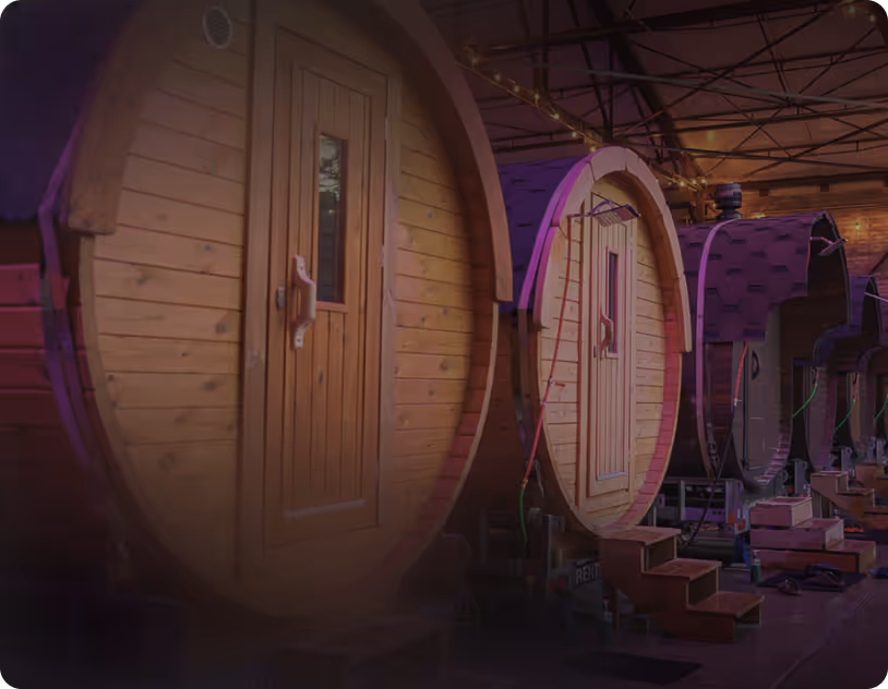 Row of wooden barrel-shaped sauna cabins with doors and small wooden steps indoors.