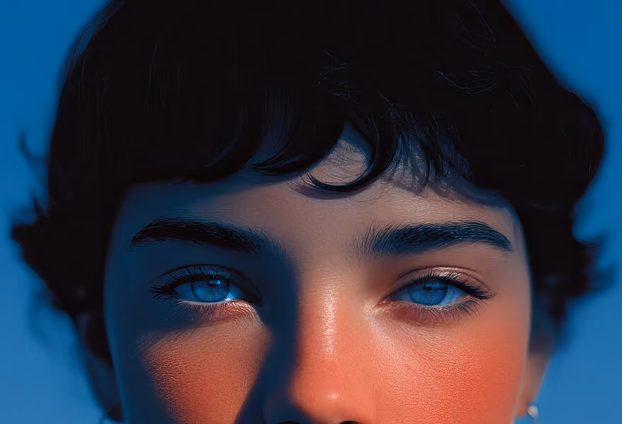 A close-up portrait of a person with striking blue eyes, short dark hair, and a serene expression, set against a gradient blue background.