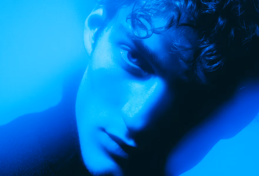 Artistic portrait of a person in dramatic blue lighting, highlighting their curly hair and creating a mysterious, surreal atmosphere.