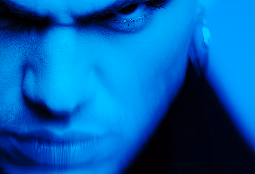 Close-up of a face in intense blue lighting, focusing on expressive eyes and dramatic shadows for a striking, artistic effect.