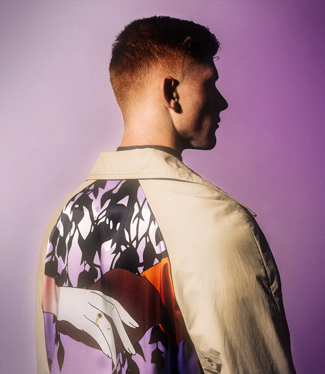 Back view of a model wearing a beige Mackintosh coat with a large illustrated floral hand-print panel from PSEUDONYM Spring Summer 2020.