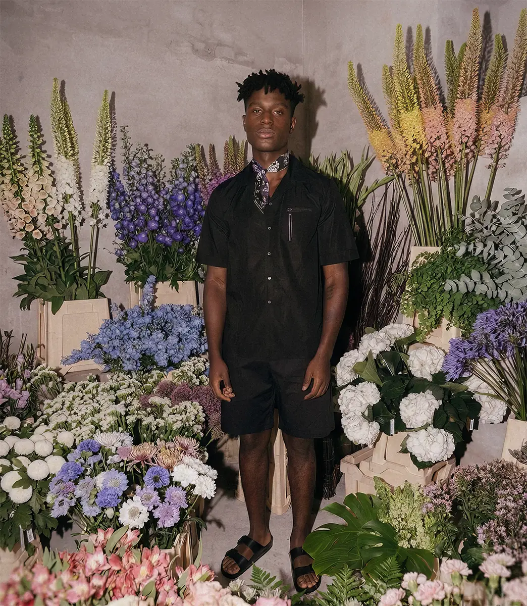 Model wearing an all-black PSEUDONYM Spring Summer 2020 look standing inside a floral installation during Copenhagen Fashion Week.
