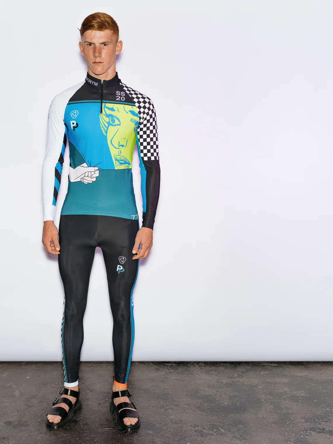 Model wearing the PSEUDONYM Spring Summer 2020 graphic compression set featuring a checkerboard sleeve, illustrated panel, and black raglan tights.