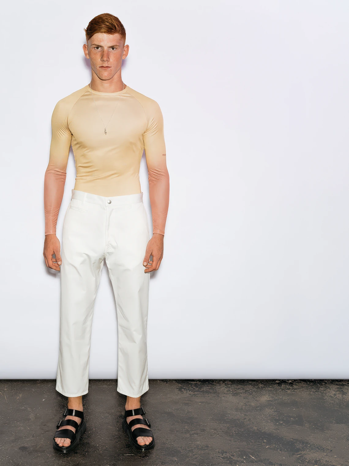 Model wearing the PSEUDONYM Spring Summer 2020 nude long-sleeve top with white trousers and black sandals.
