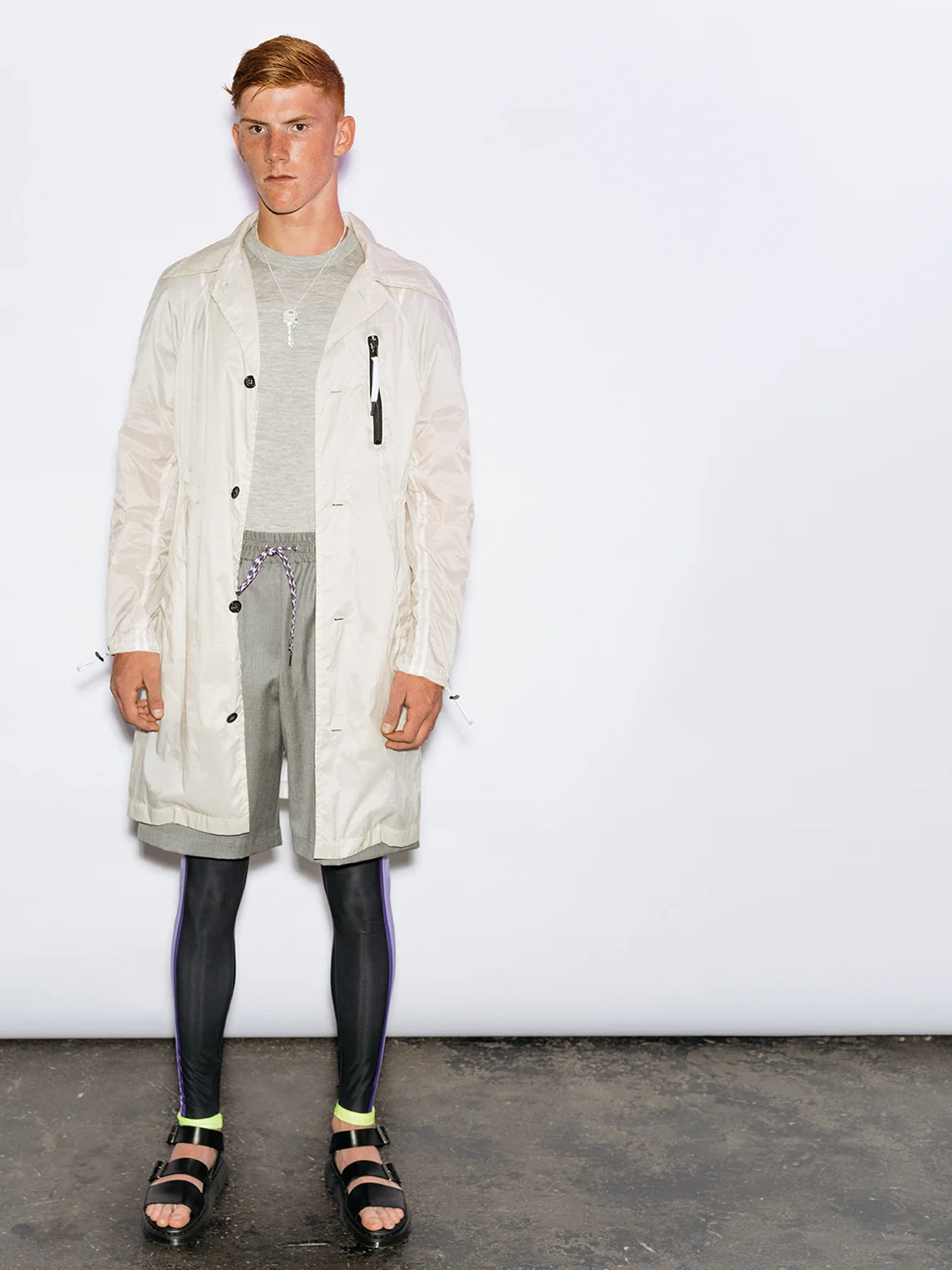 Model wearing the PSEUDONYM Spring Summer 2020 translucent white technical field coat over grey base layers, styled with black leggings featuring neon cuff details.