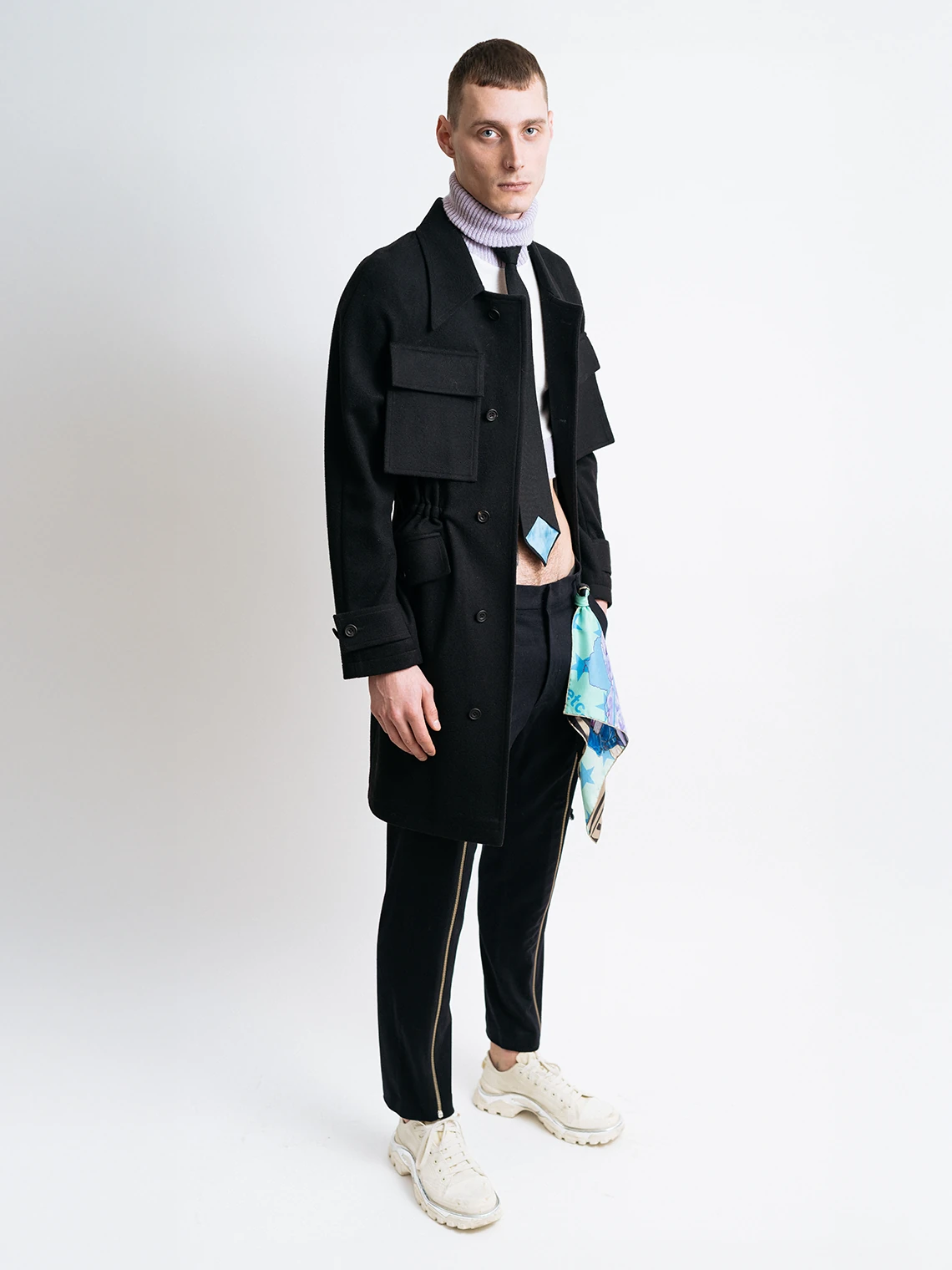 Model wearing a black field coat over a cropped knit top, with slim black trousers and a silk scarf detail for PSEUDONYM Autumn Winter 2019.
