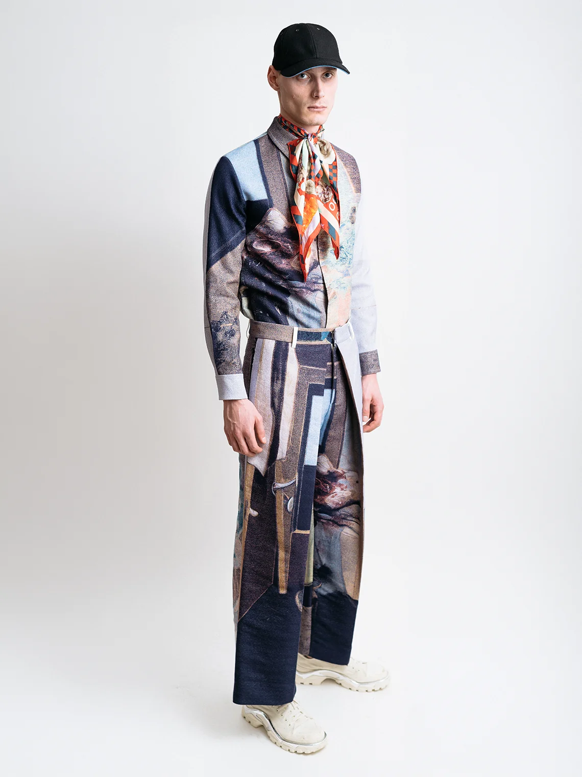 Model wearing a matching jacquard shirt and pleated trousers with a silk scarf and black cap for PSEUDONYM Autumn Winter 2019.