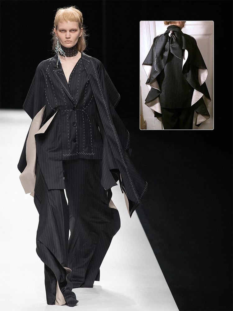 Runway look with a black pinstripe tailored jacket, wide draped panels, loose trousers, visible tack lines, and a back-view inset.