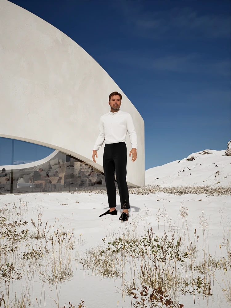 Man standing in a snowy landscape outside a curved white gallery building under a blue sky.