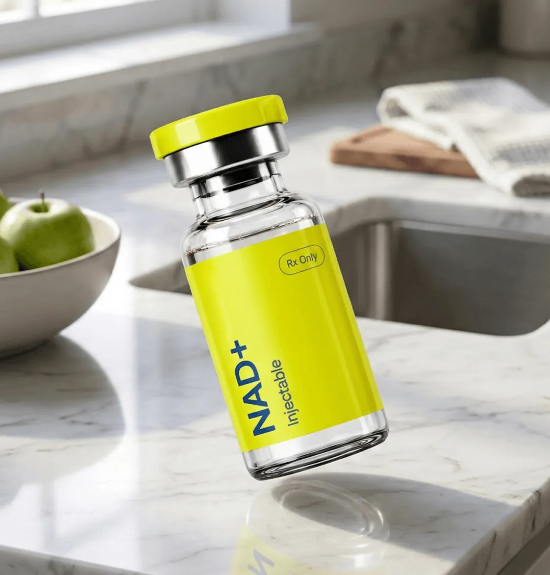 Clear glass vial labeled NAD+ Injectable with yellow cap and label on a marble kitchen counter.