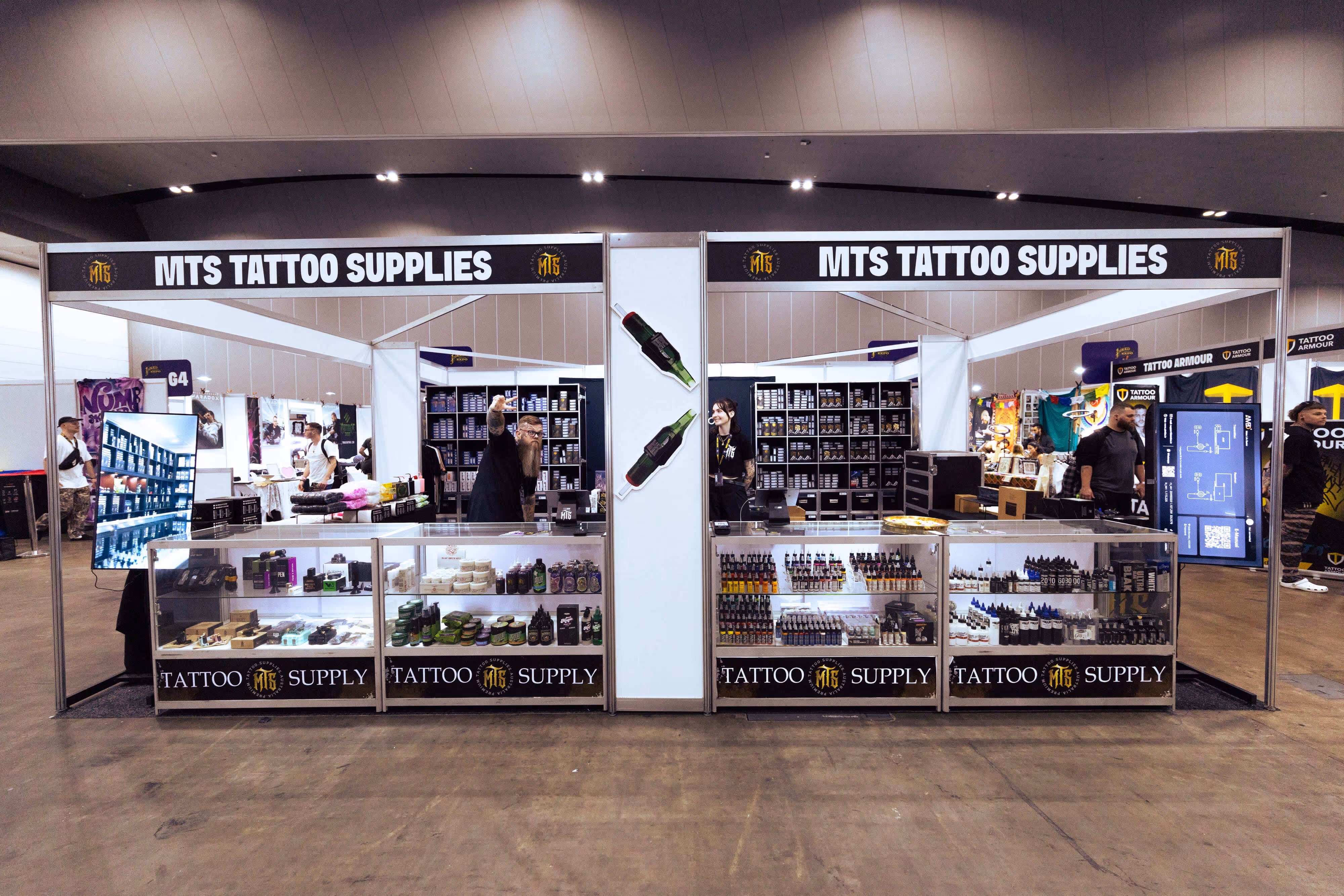 MTS Tattoo Supplies booth with glass display cases filled with tattoo inks and products at a convention.