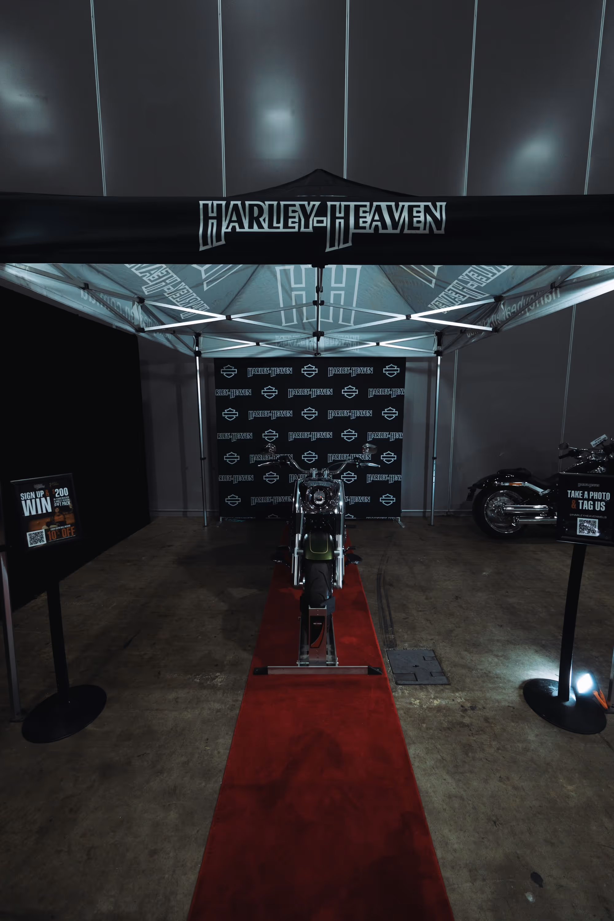 Motorcycle displayed under a black canopy with 'Harley-Heaven' branding and a red carpet leading up to it.
