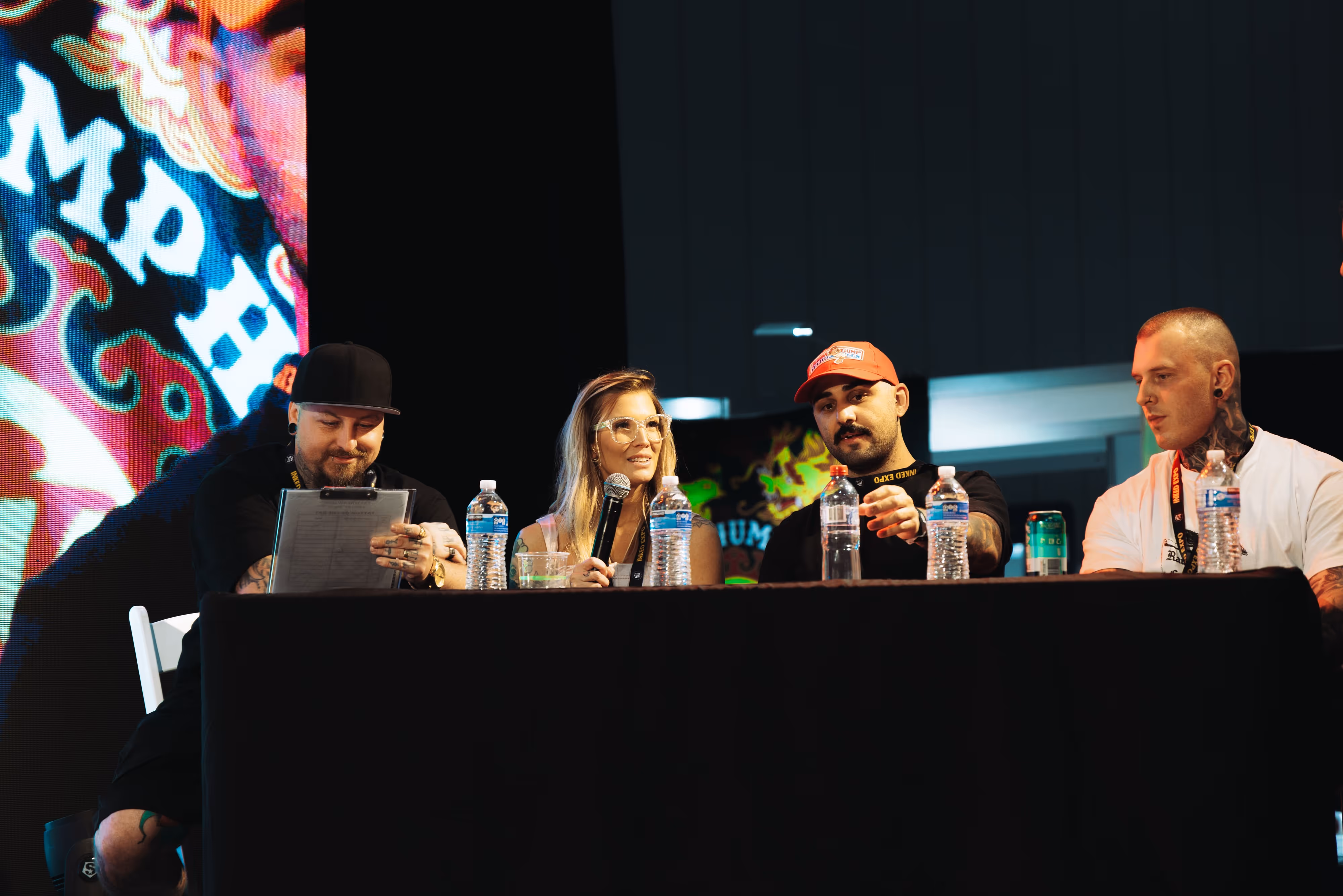 Four people sitting at a panel table with microphones and water bottles during a discussion or event.