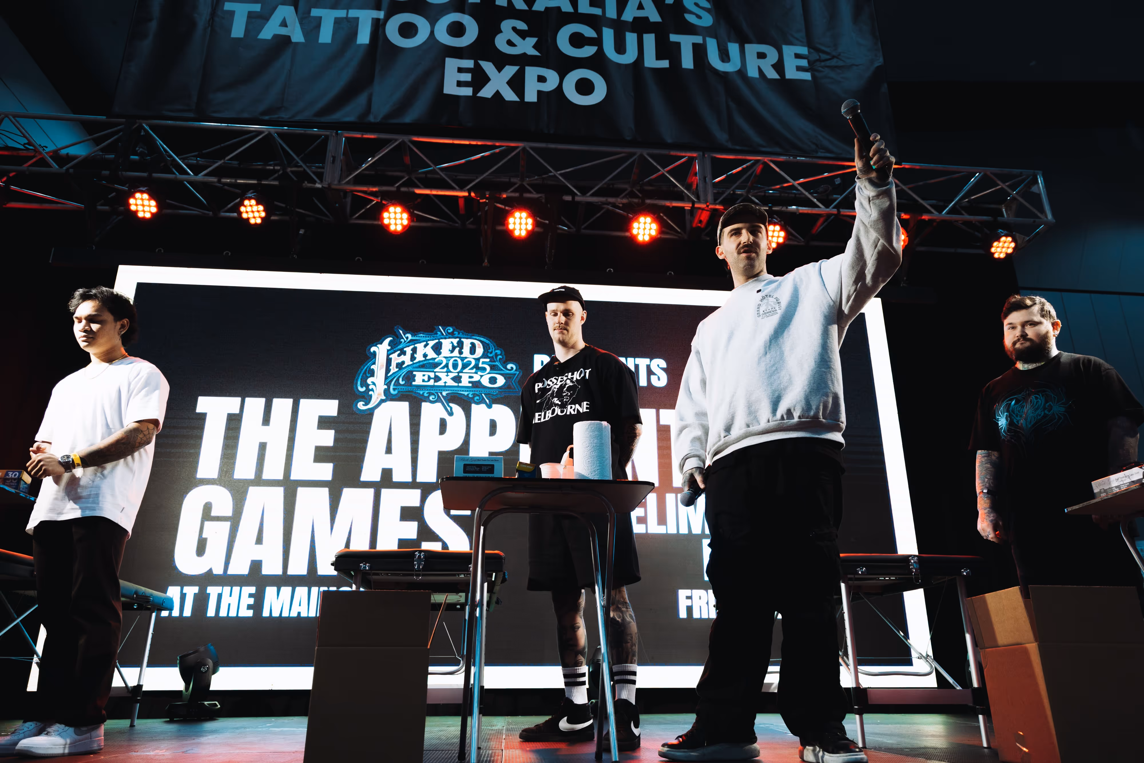 Four men standing on stage at Australia's Tattoo & Culture Expo 2025 with one holding a microphone.