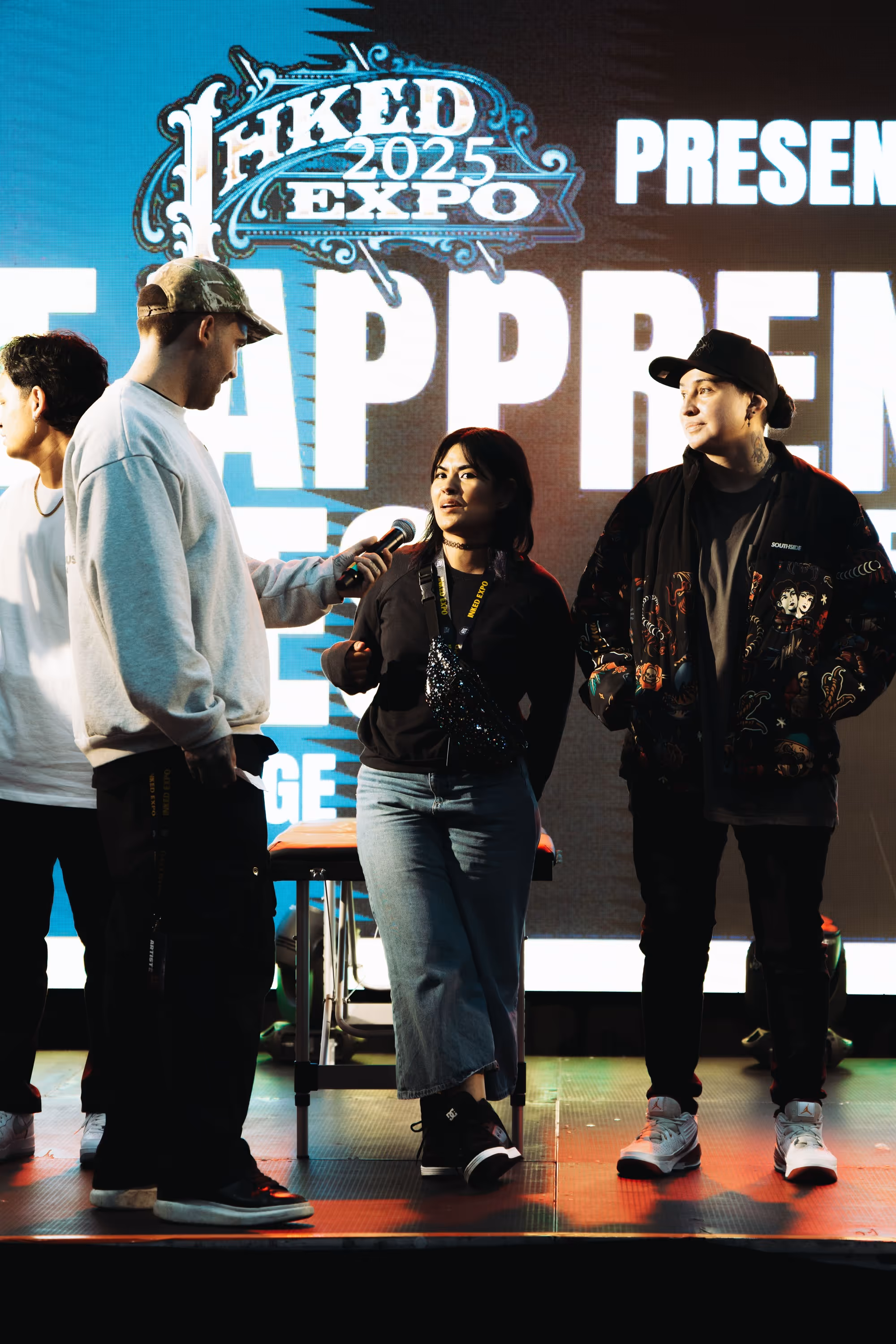 Four people on stage at Inked 2025 Expo, one holding a microphone interviewing a woman in a black top and jeans.