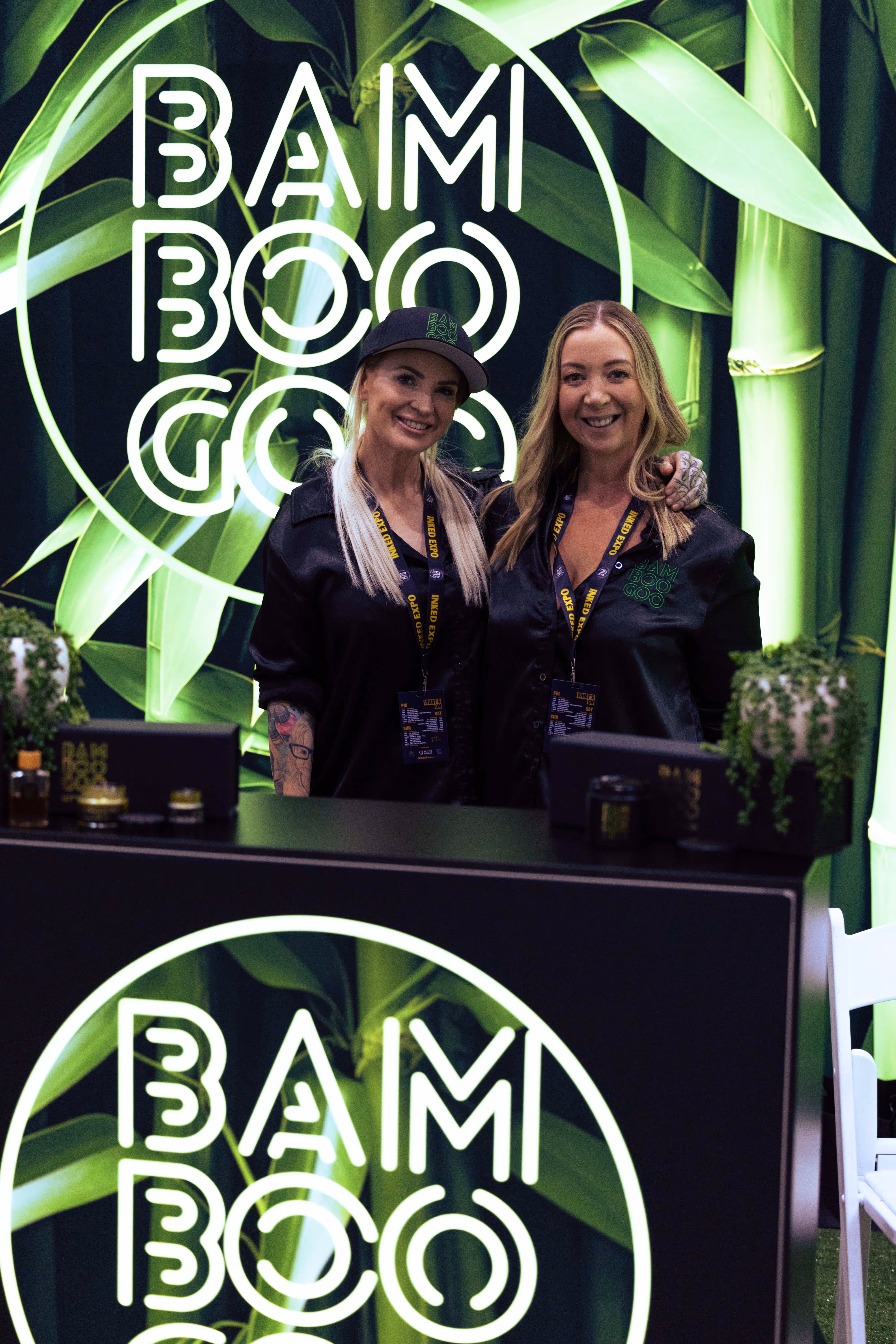 Two smiling women standing behind a counter with Bamboo Goo logos and a green bamboo leaf backdrop.