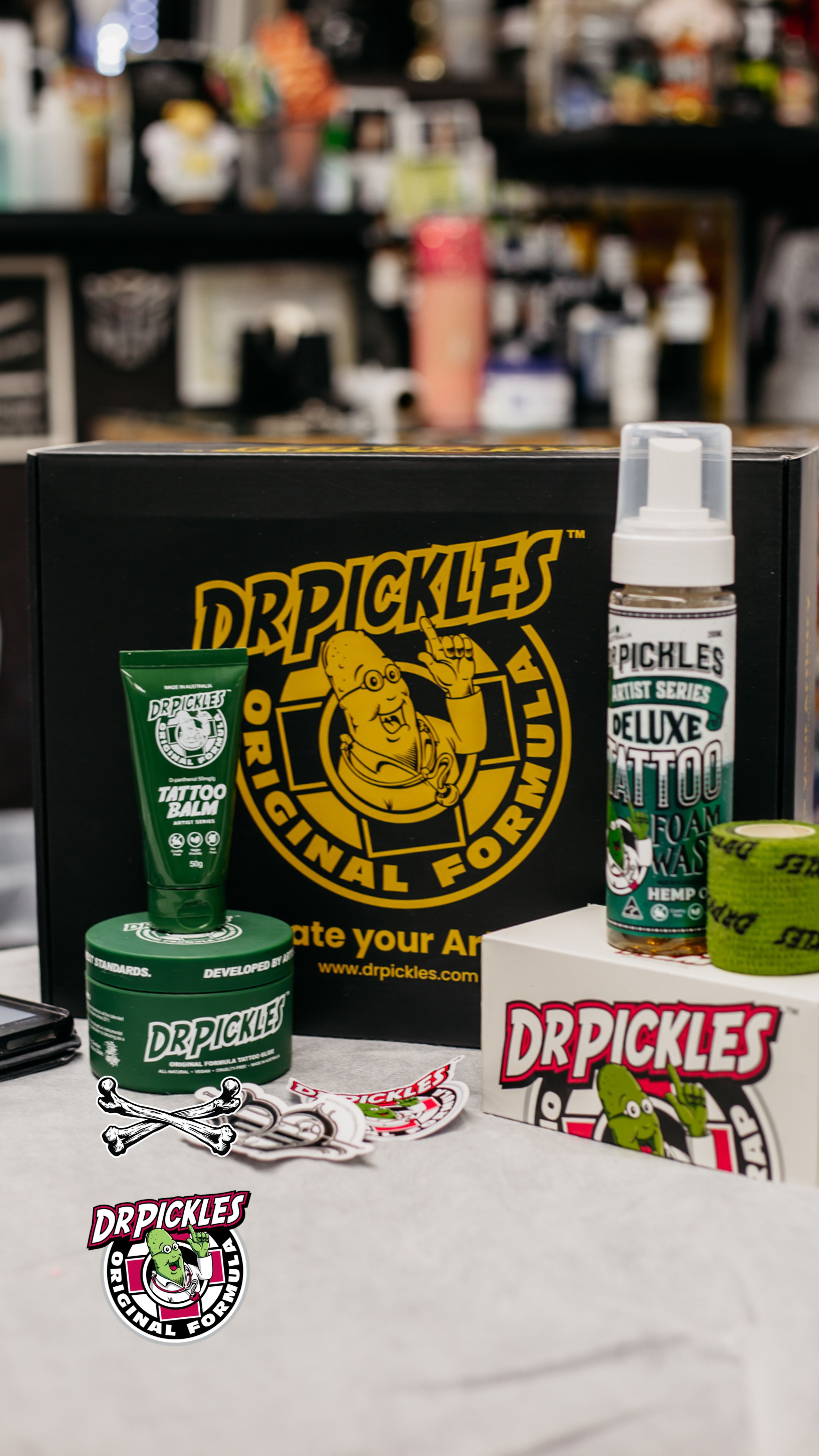 Dr. Pickles tattoo products including green tattoo balm, deluxe tattoo foam wash, adhesive tape, and a large black box with yellow branding.