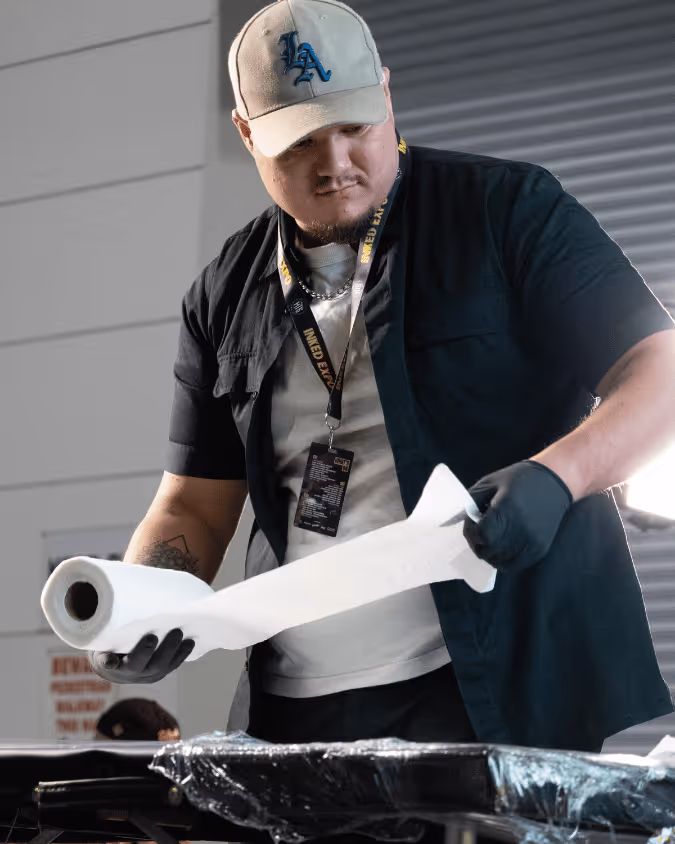 Man wearing black gloves and a cap holding and unrolling a roll of white paper towels indoors.