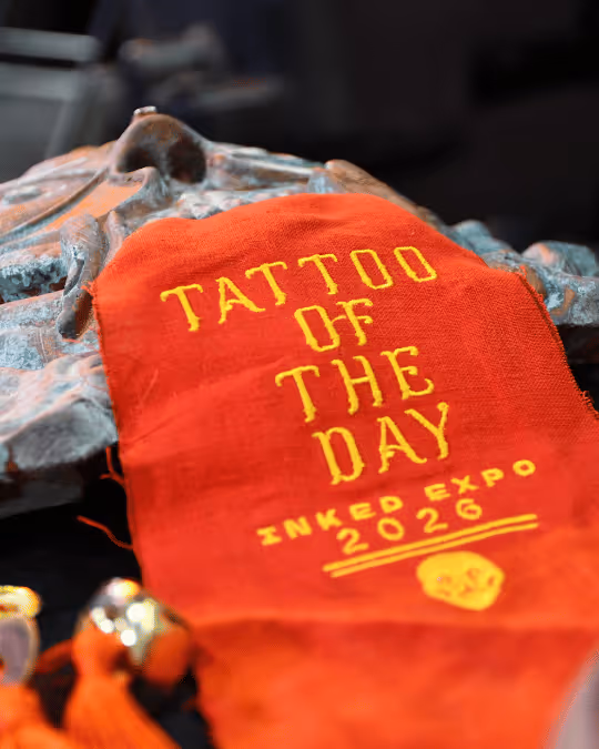 Red fabric patch with yellow text reading 'Tattoo of the Day Inked Expo 2026' and a small skull graphic at the bottom.
