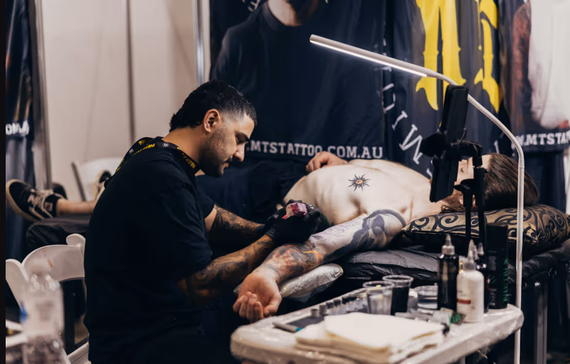 Tattoo artist working on a tattoo sleeve for a shirtless man lying on a table in a tattoo studio.