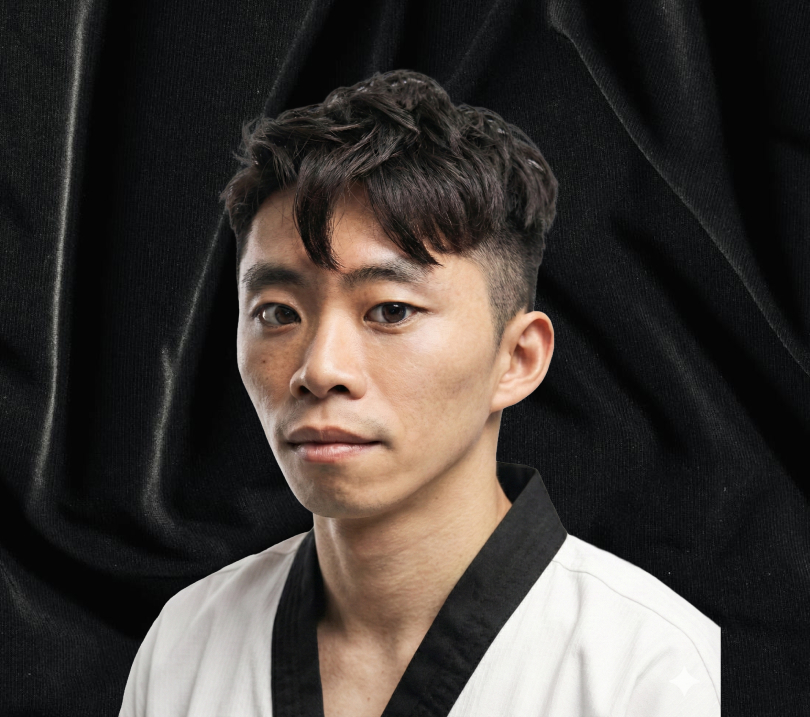 Portrait of a young man with short dark hair wearing a white martial arts uniform with black collar against a black fabric background.