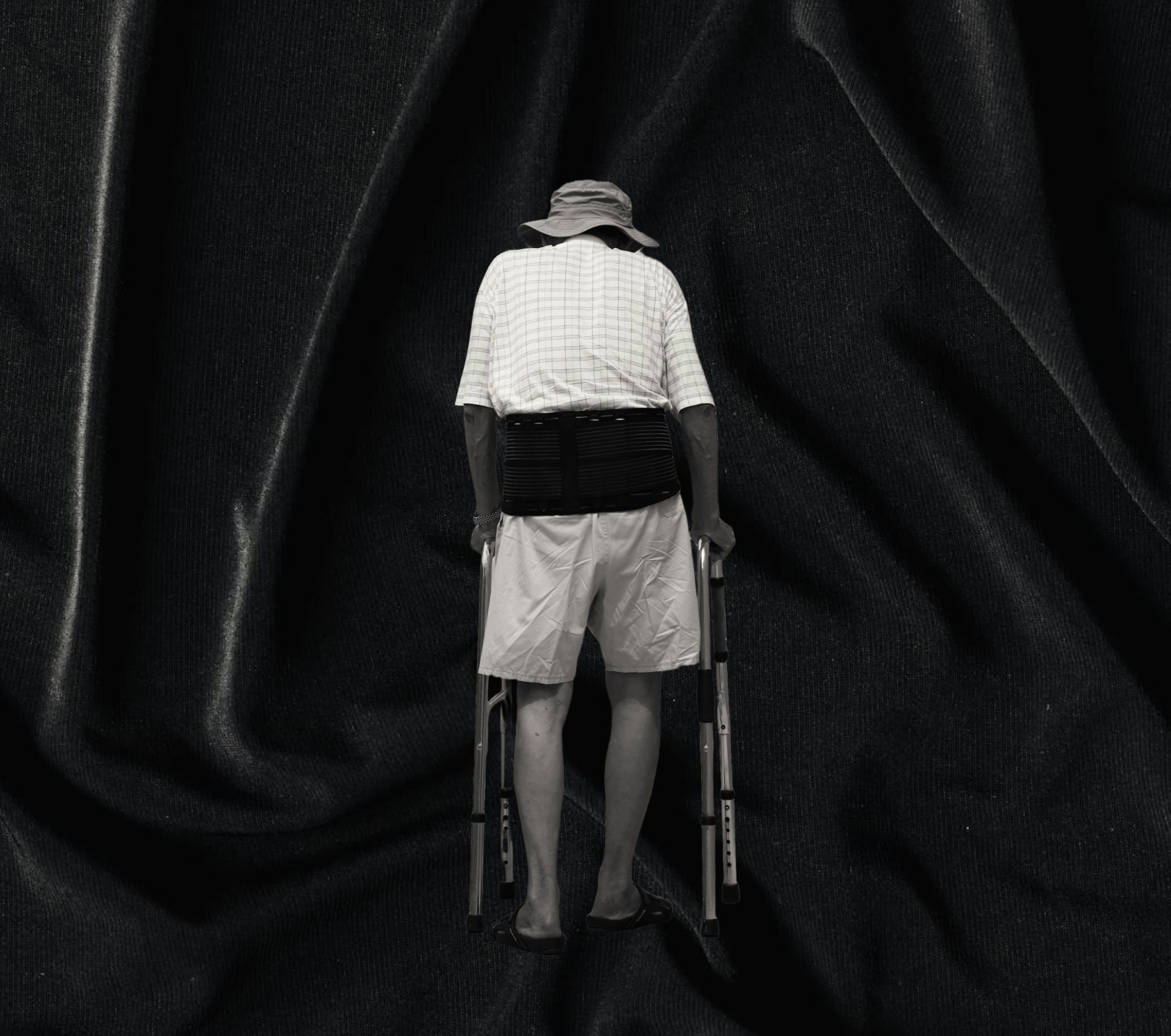 Man wearing a bucket hat and back brace using crutches on a black fabric background.