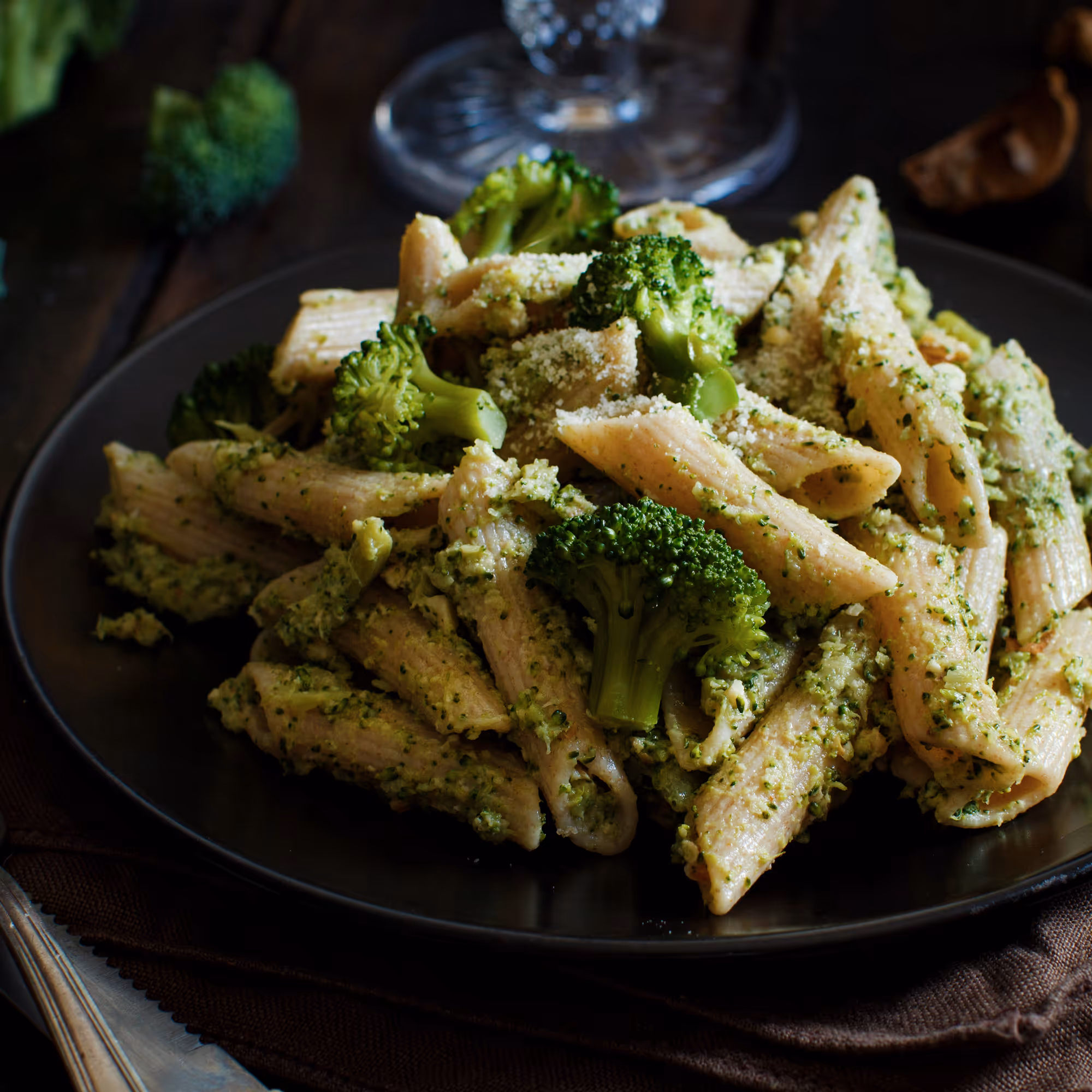Plate of penne pasta mixed with broccoli florets and green pesto sauce, sprinkled with grated cheese.