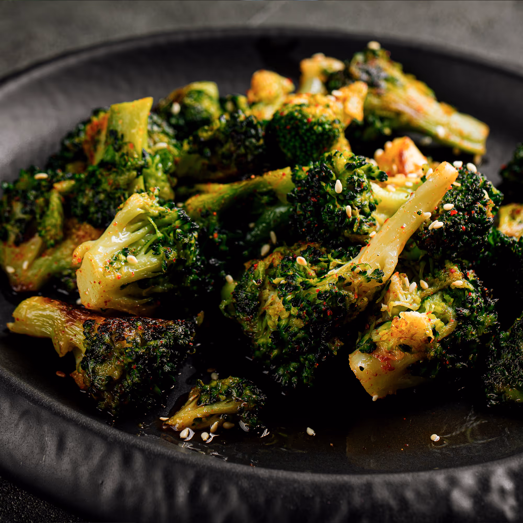 Close-up of roasted broccoli florets garnished with sesame seeds on a dark plate.