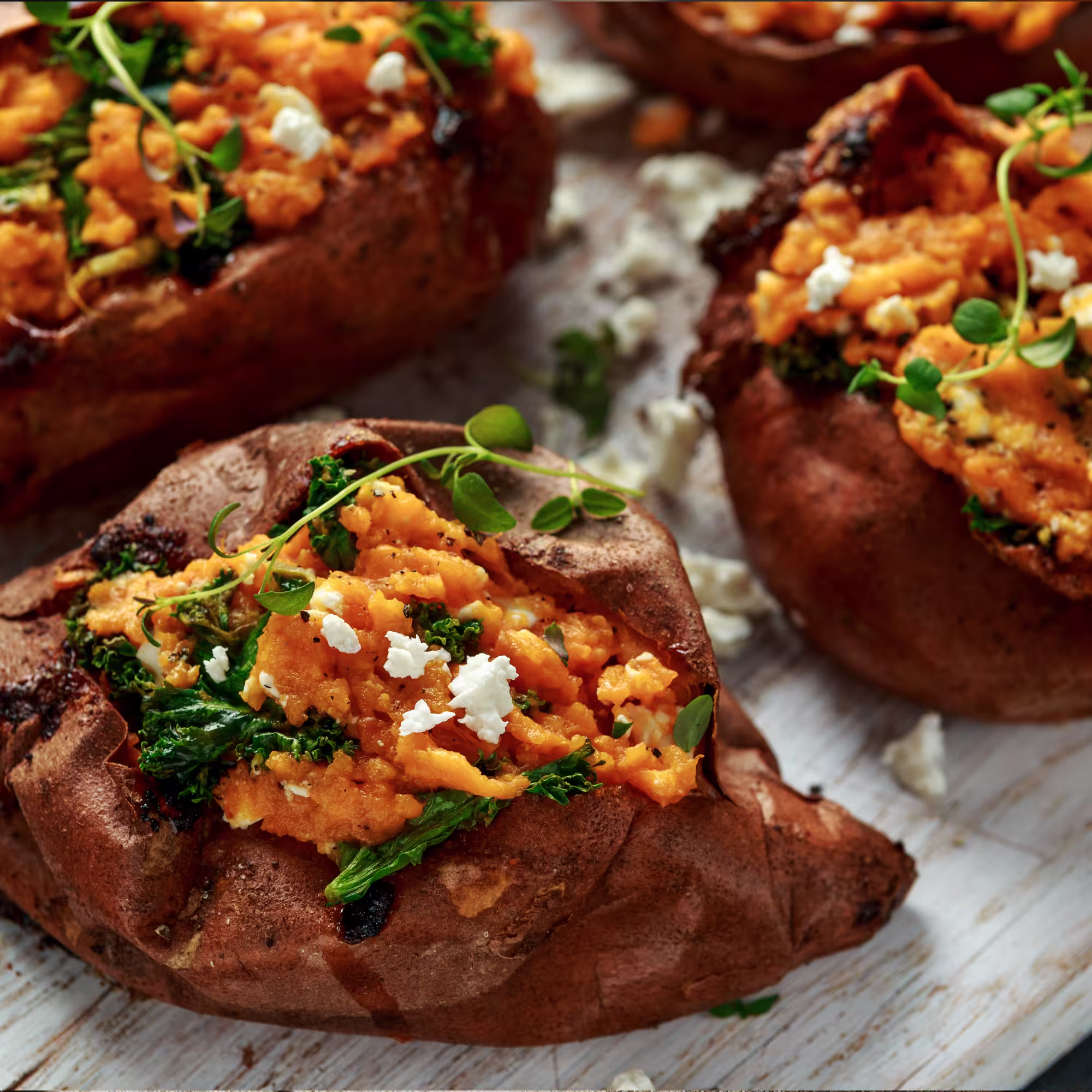 Baked sweet potatoes stuffed with mashed orange sweet potato, kale, crumbled white cheese, and garnished with fresh herbs.
